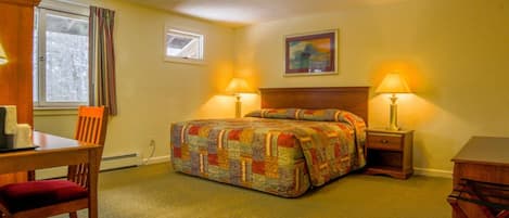 A hotel room with a bed, two bedside lamps, a desk with a chair, a window with curtains, and a painting on the wall.