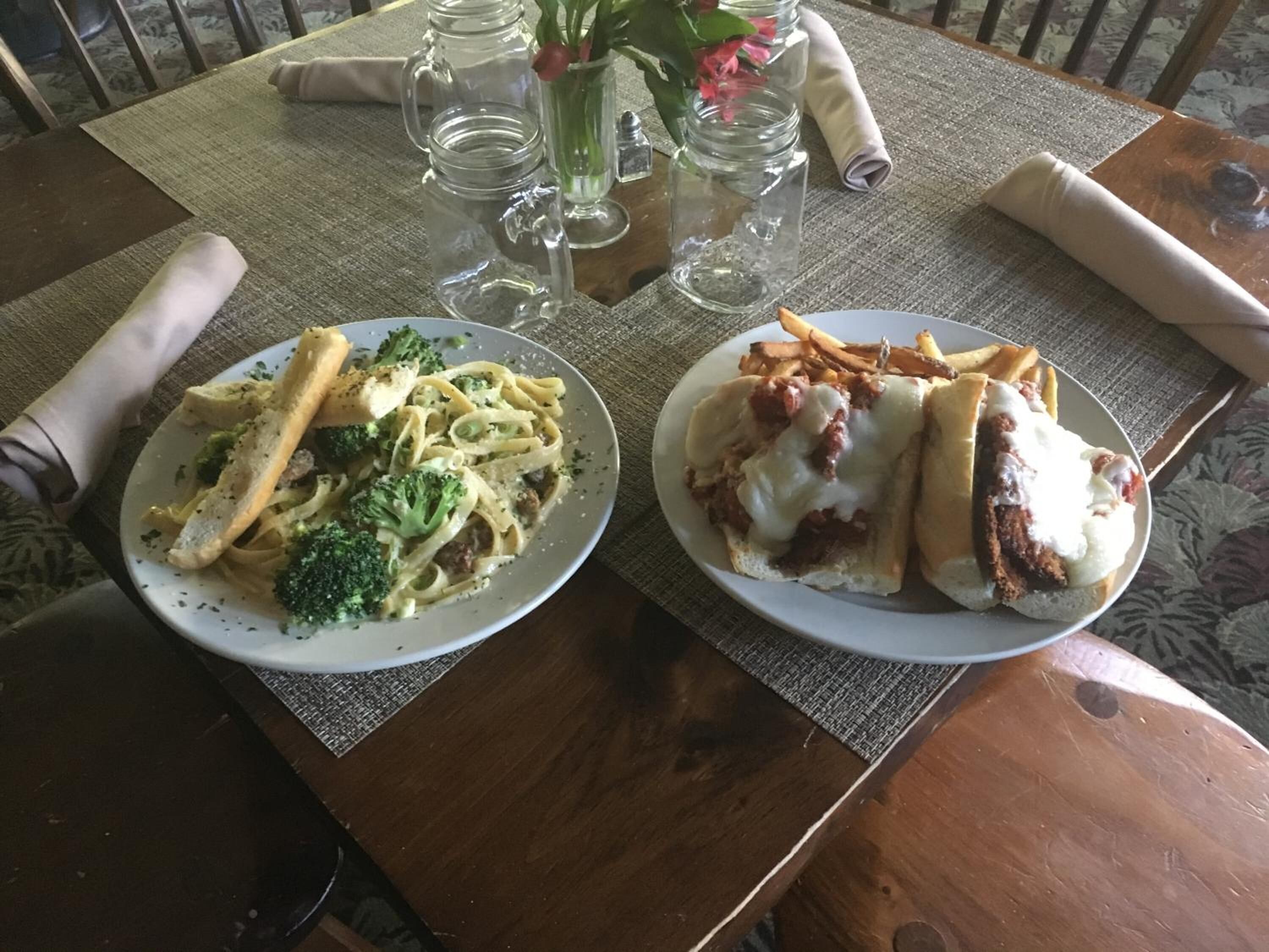 Two plates of pasta and sandwiches on a table with a placemat.