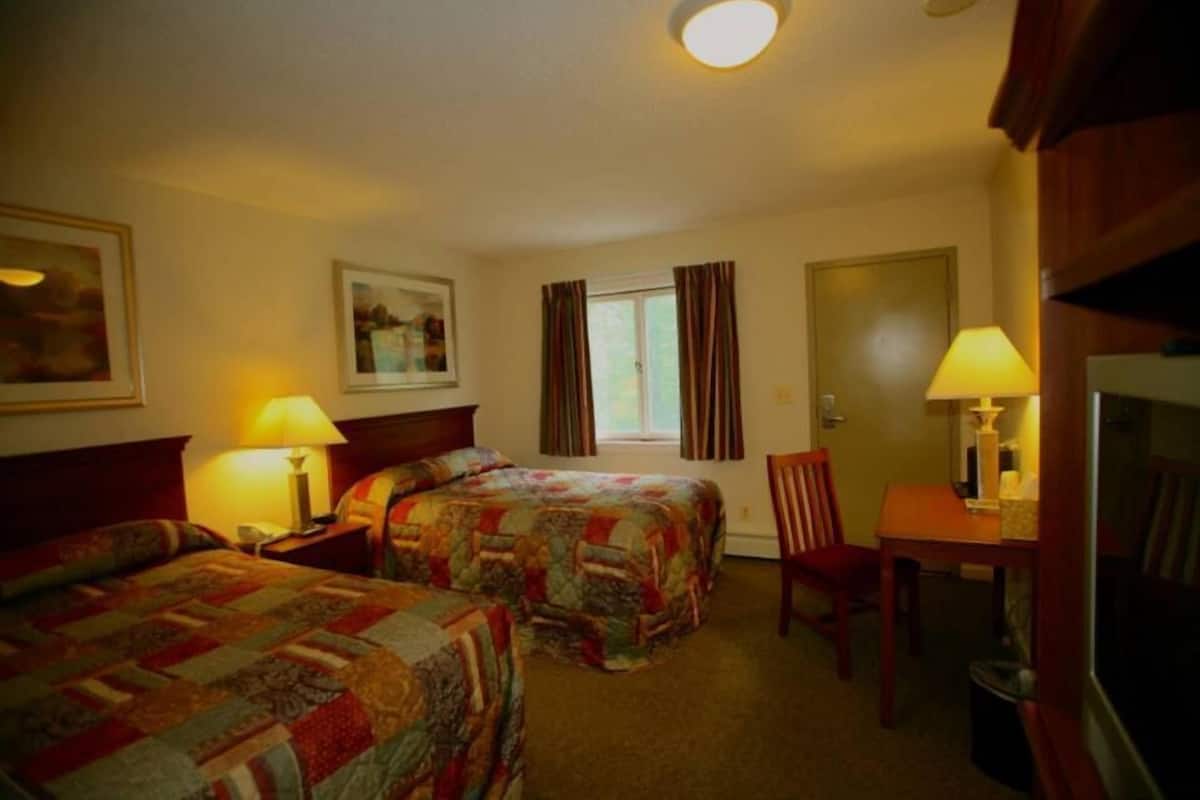 A hotel room with two beds, a desk, a chair, and a television.