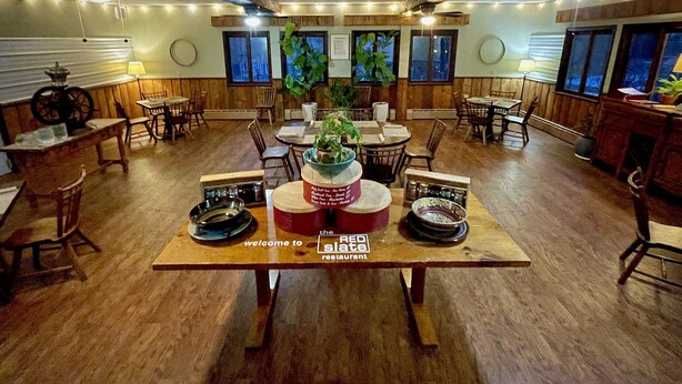 A restaurant with wooden tables and chairs, a central table with a sign reading "The Red Slate Restaurant", and large windows with views of the outside. - The Upper Pass Lodge at Magic Mountain (Londonderry)