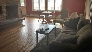 A living room with a fireplace, a sofa, a coffee table, and a dining area with chairs and a table. - The Upper Pass Lodge at Magic Mountain (Londonderry)