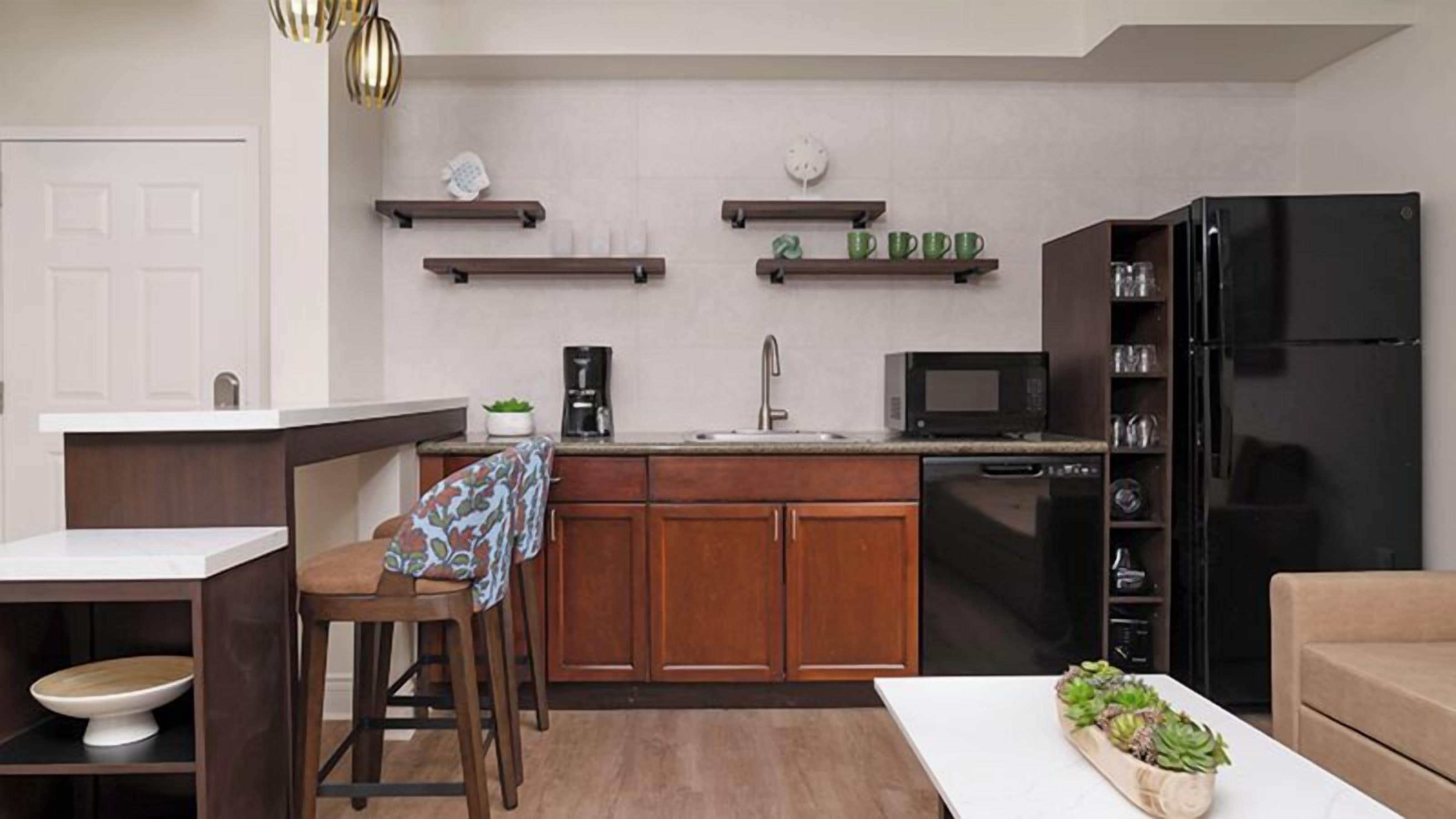 A compact kitchen with wooden cabinets, a black refrigerator, a microwave, and a coffee maker.