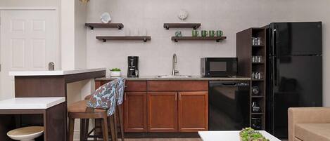 Una cocina compacta con armarios de madera, un refrigerador negro, un microondas y una cafetera.