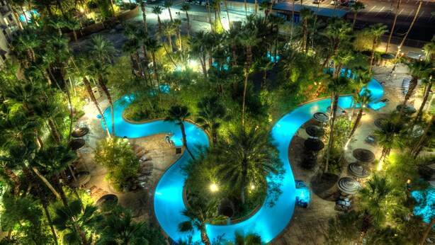 An aerial view of a resort with a winding pool surrounded by palm trees and outdoor seating areas. - Tahiti Village Resort & Spa (Las Vegas)