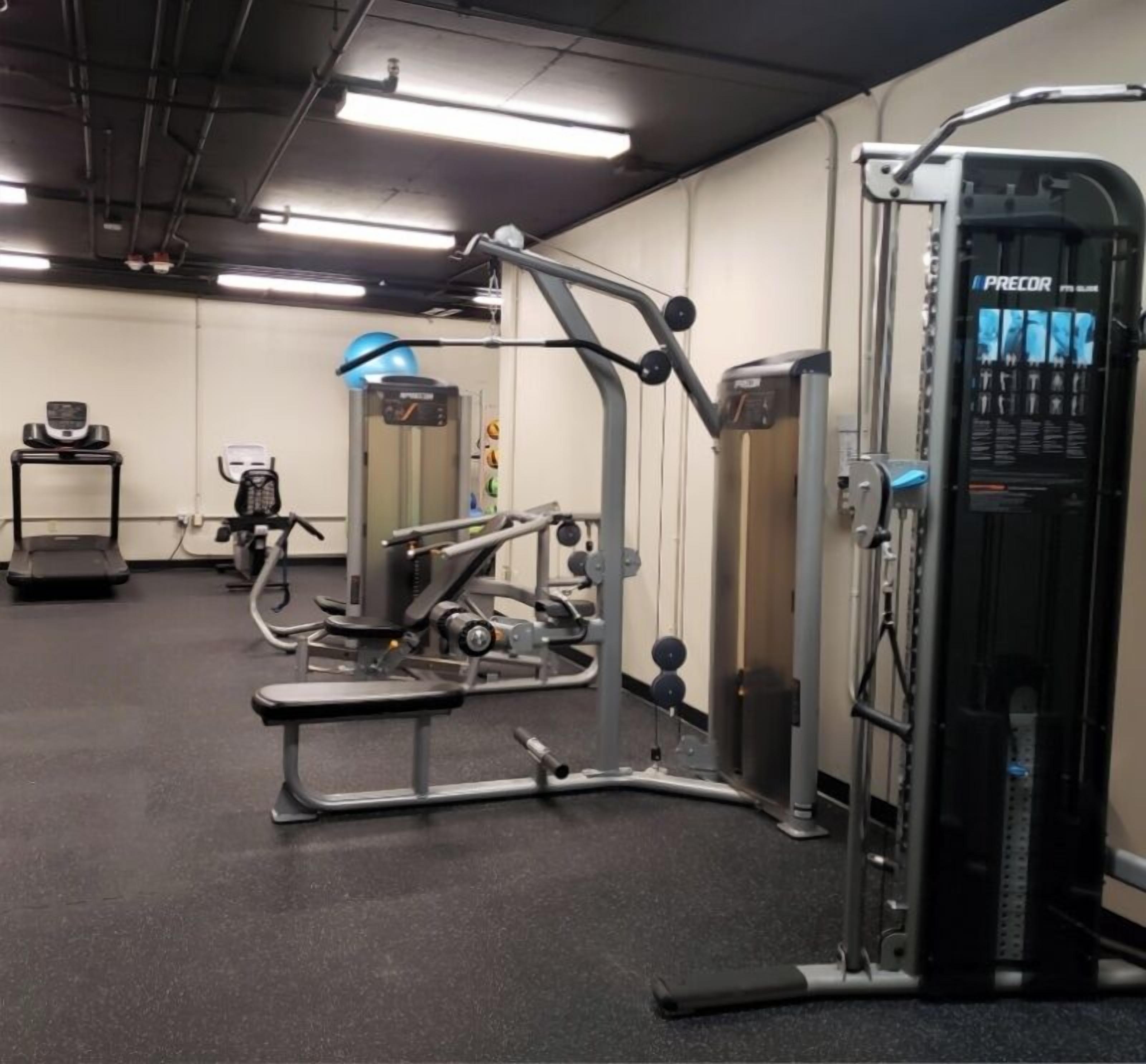 Un gimnasio con diferentes máquinas de ejercicio, una cinta de correr y una pantalla instalada en la pared.
