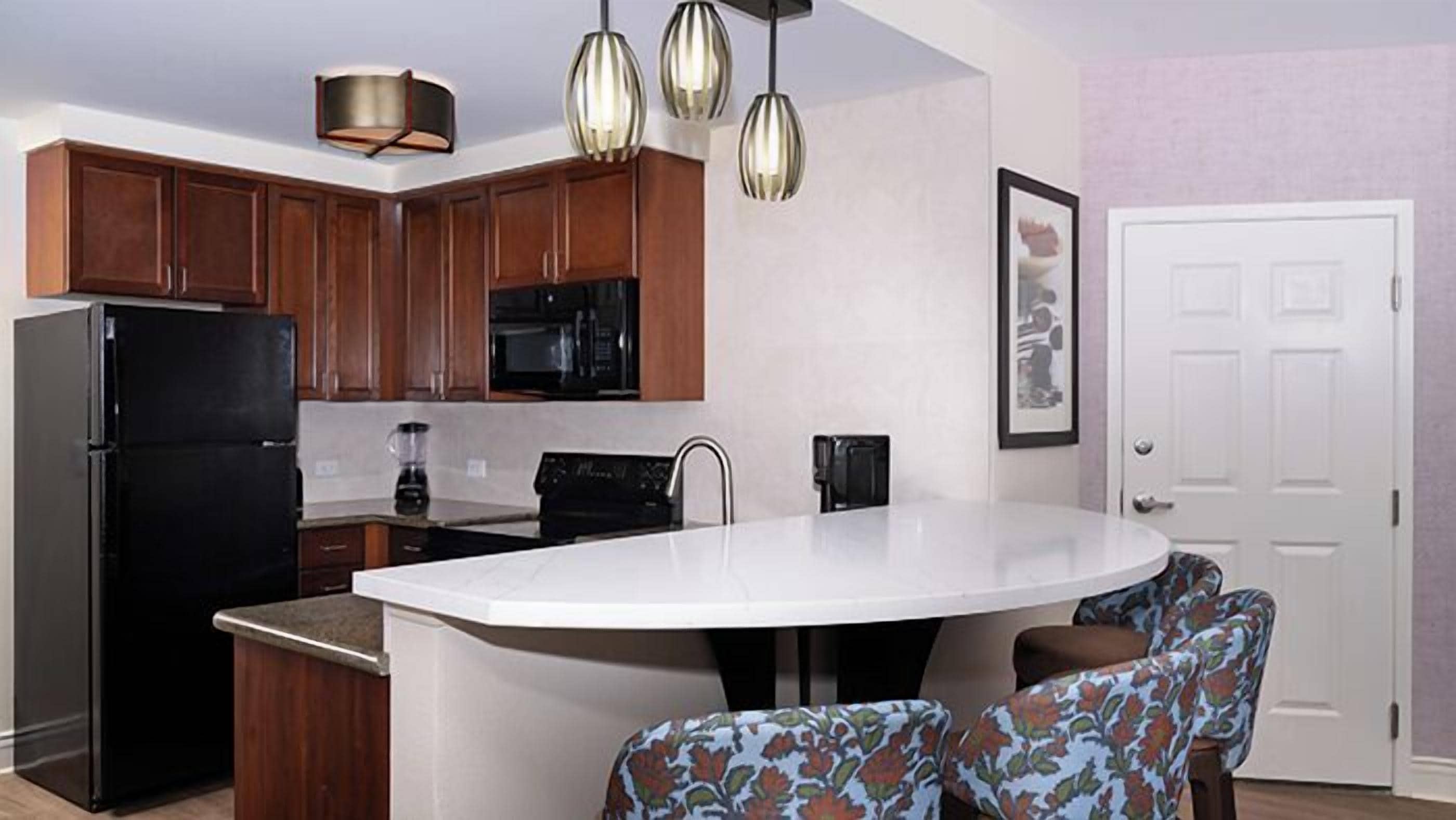 A modern kitchen with wooden cabinets, a black refrigerator, a microwave, a coffee maker, and a large island with chairs.