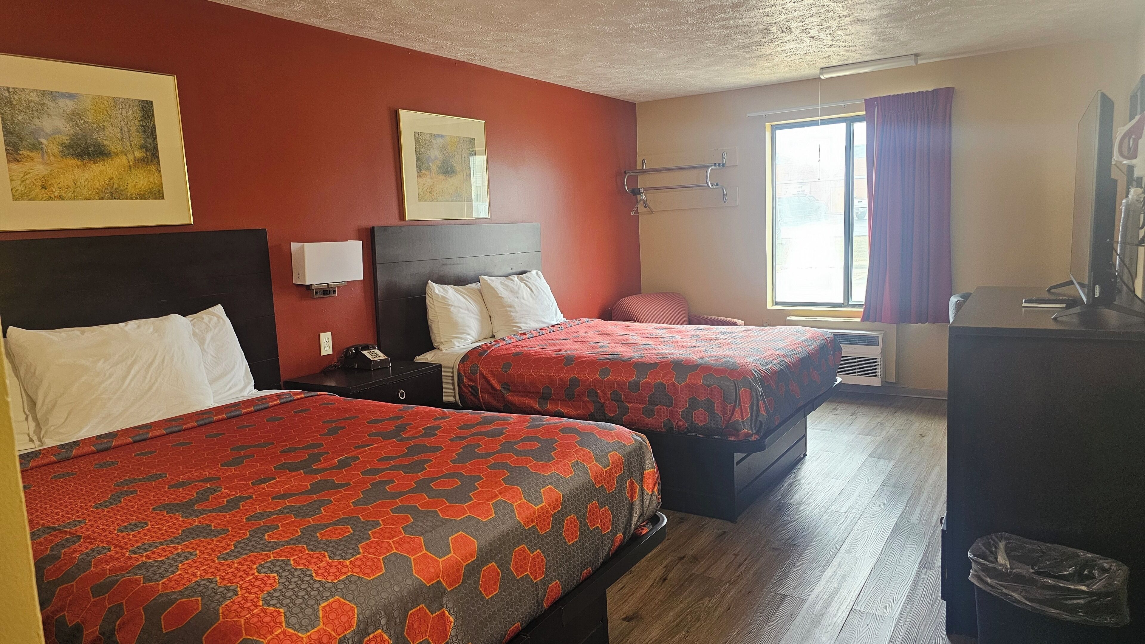 A hotel room with two beds, a desk, a chair, a TV, and a window with curtains.