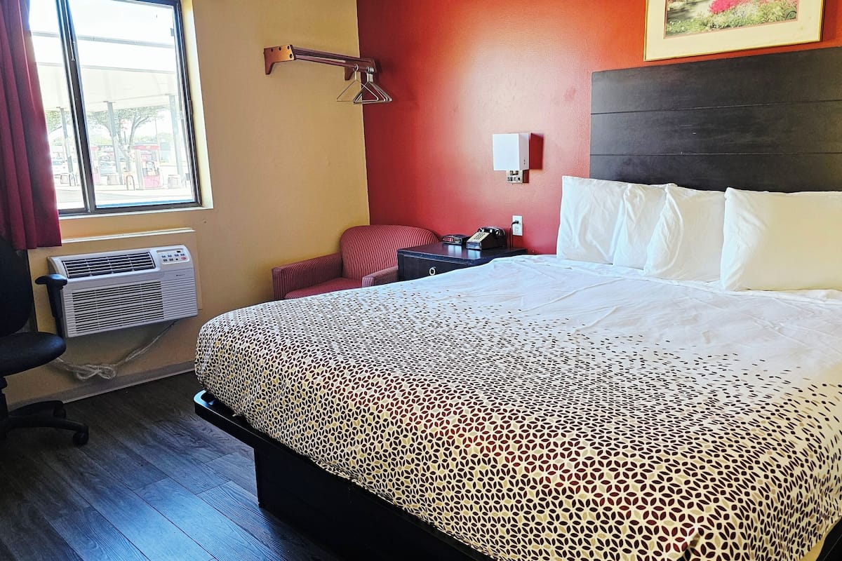 A hotel room with a bed, a chair, a desk, and an air conditioning unit.