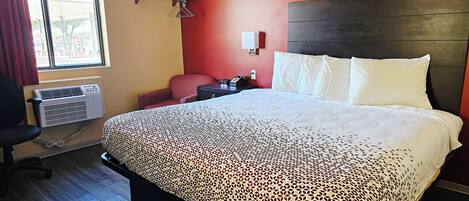 A hotel room with a bed, a chair, a desk, and an air conditioning unit.