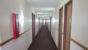 A hotel hallway with a checkered floor, doors on both sides, and a red emergency phone on the left.