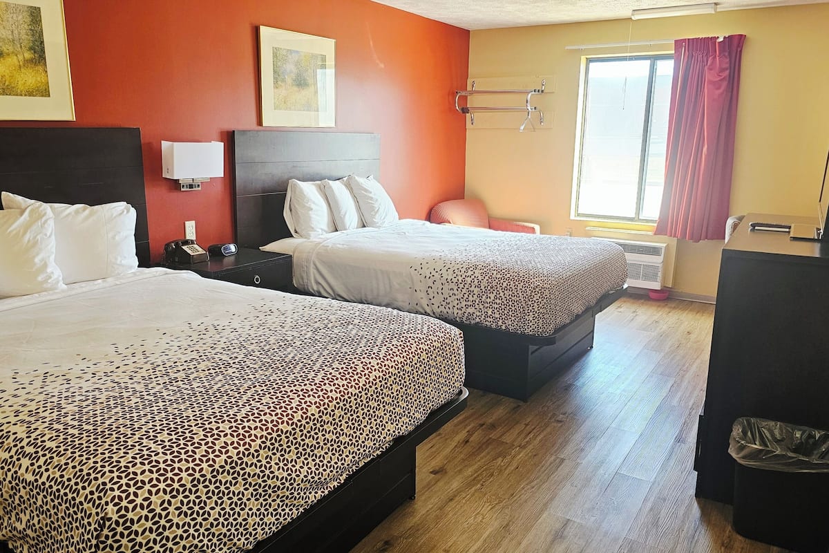 A hotel room with two beds, a desk, a chair, a TV, and a window with curtains.