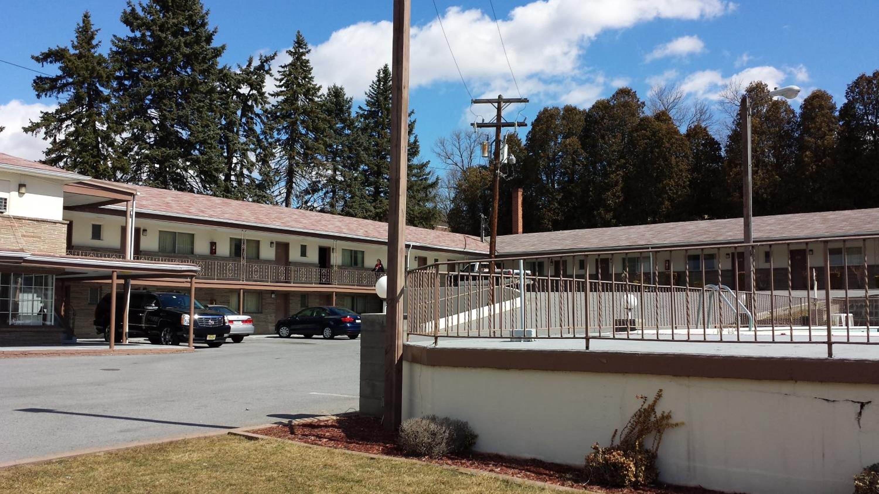 Um motel com estrutura em dois andares, área de estacionamento coberta e espaço ao ar livre cercado.