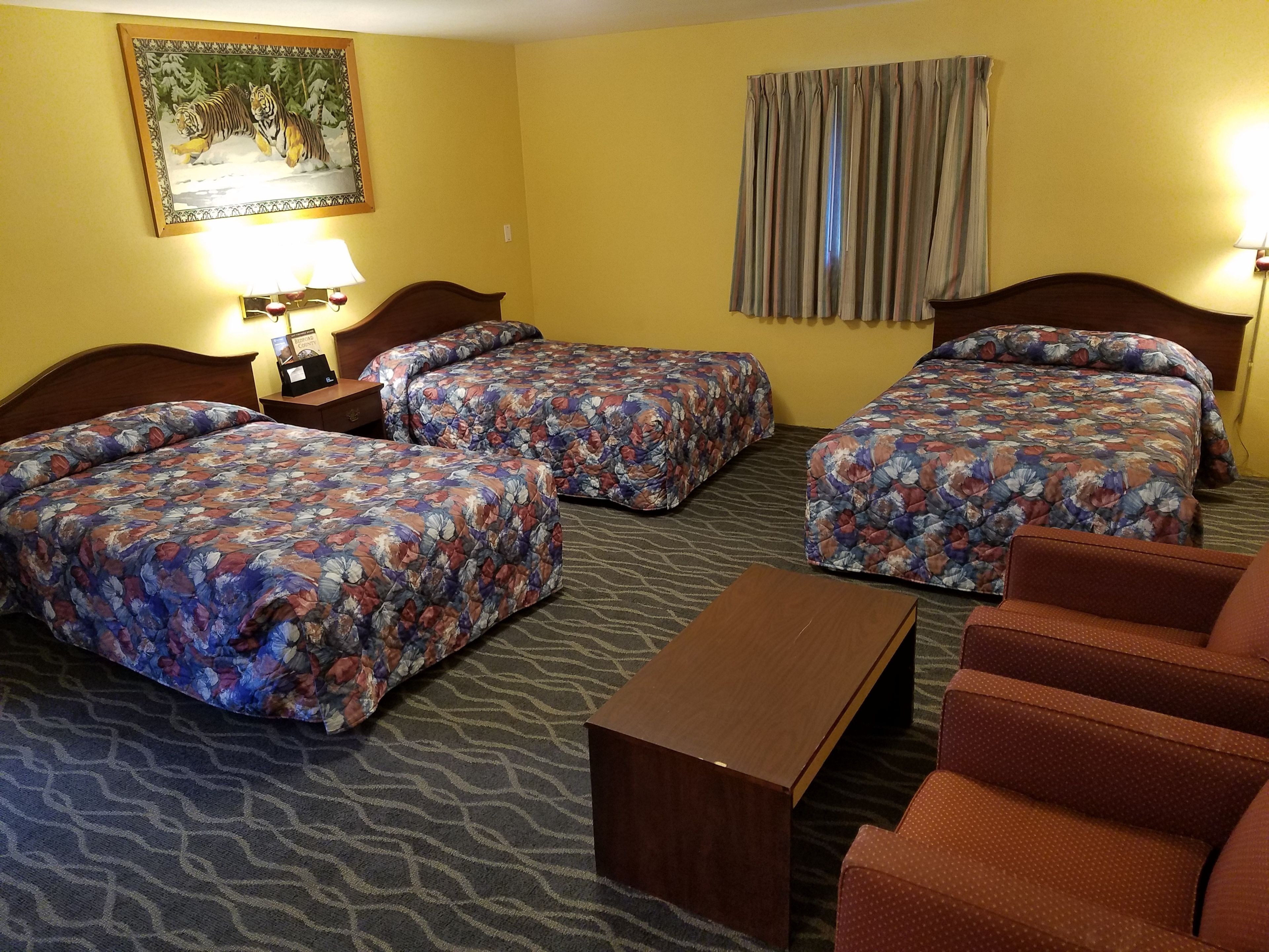A hotel room with three beds, a wooden nightstand, a small table, and a chair.
