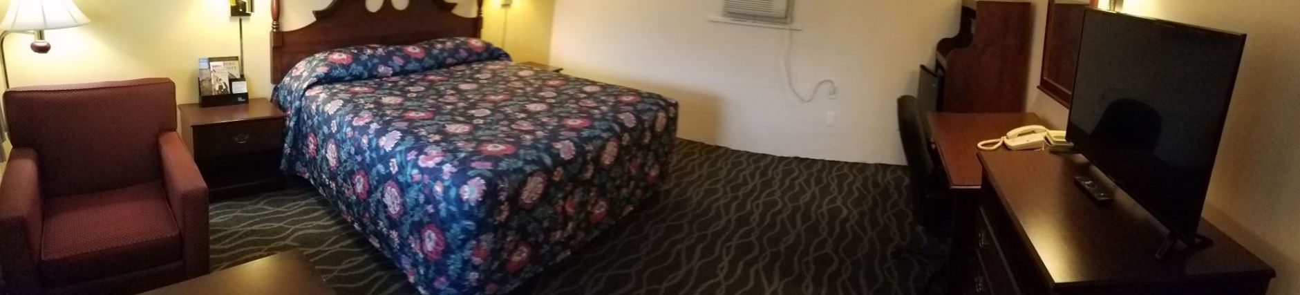 Une chambre d’hôtel comprenant un lit, un bureau avec un téléphone, une chaise et un téléviseur.