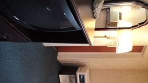 A compact room with a bed, a desk, a chair, a radiator, and a window. - Budget Host Midway Inn (Bedford)