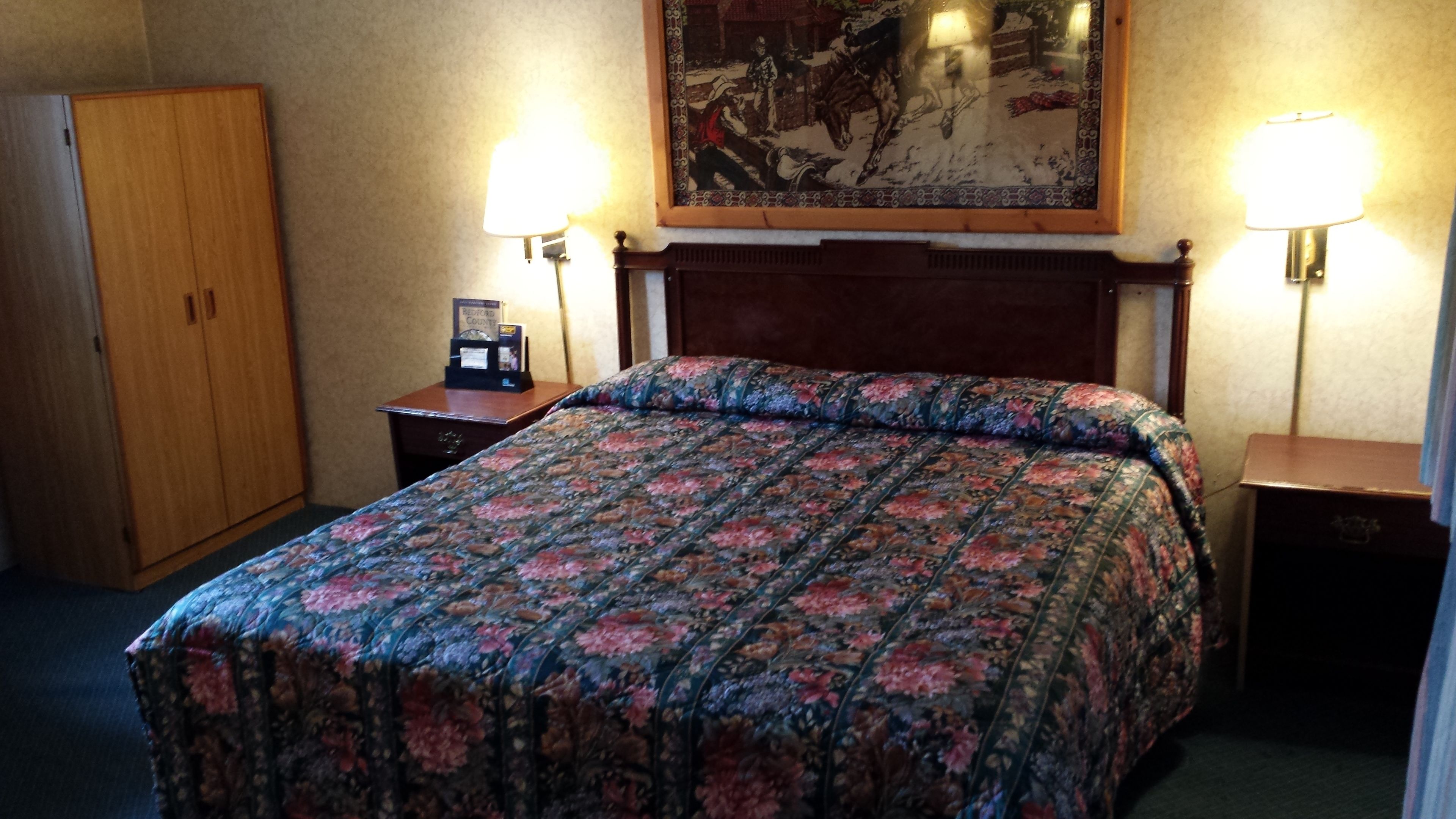 Una camera d'albergo con un letto, un comodino, un armadio in legno e un quadro appeso al muro.