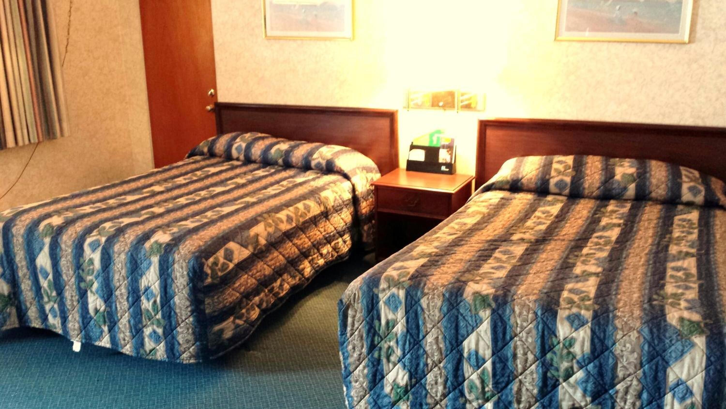 A hotel room with two single beds, a nightstand with a lamp, and a door.