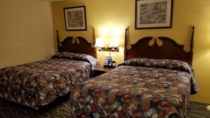 A hotel room with two beds, each with a floral bedspread, a nightstand with a lamp, and two framed pictures on the wall. - Budget Host Midway Inn (Bedford)