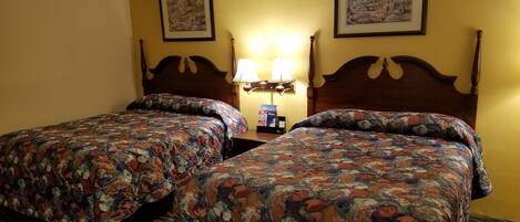 A hotel room with two beds, each with a floral bedspread, a nightstand with a lamp, and two framed pictures on the wall.