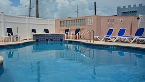 Una piscina con sillas de descanso y un muro de ladrillo con un cartel.