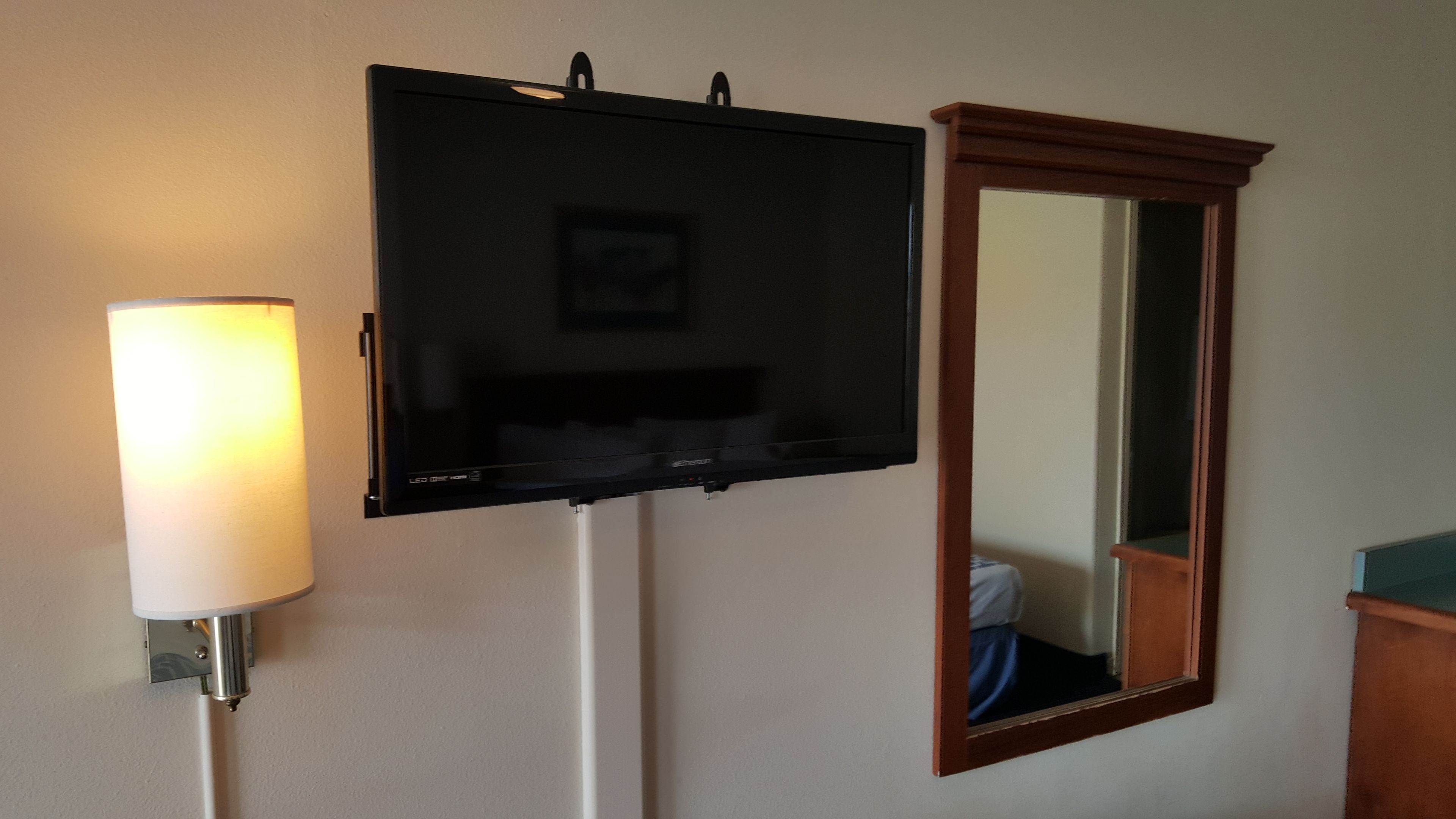 Un televisor de pantalla plana montado en la pared, una lámpara adosada a la pared y un espejo.