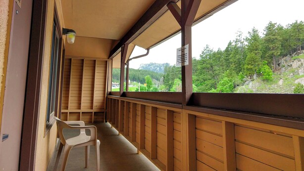 A wooden balcony with a view of a forested valley and rocky cliffs. - Magnuson Grand Rushmore View (Keystone)