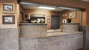 A reception area with a counter, framed pictures on the walls, and a door in the background. - Magnuson Grand Rushmore View (Keystone)