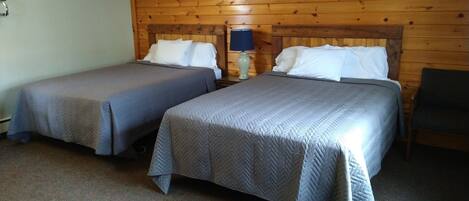 Une chambre avec deux lits, des lambris en bois sur les murs, une lampe sur la table de chevet et une chaise.