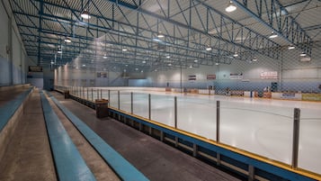 Una pista de hielo interior con techo alto y vigas metálicas, con una barrera de pista azul y amarilla y algunas bancas a lo largo de los lados.