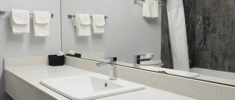 Un baño moderno con un espejo grande, lavamanos blanco y zona de ducha.