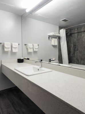 Un baño moderno con un espejo grande, lavamanos blanco y zona de ducha.