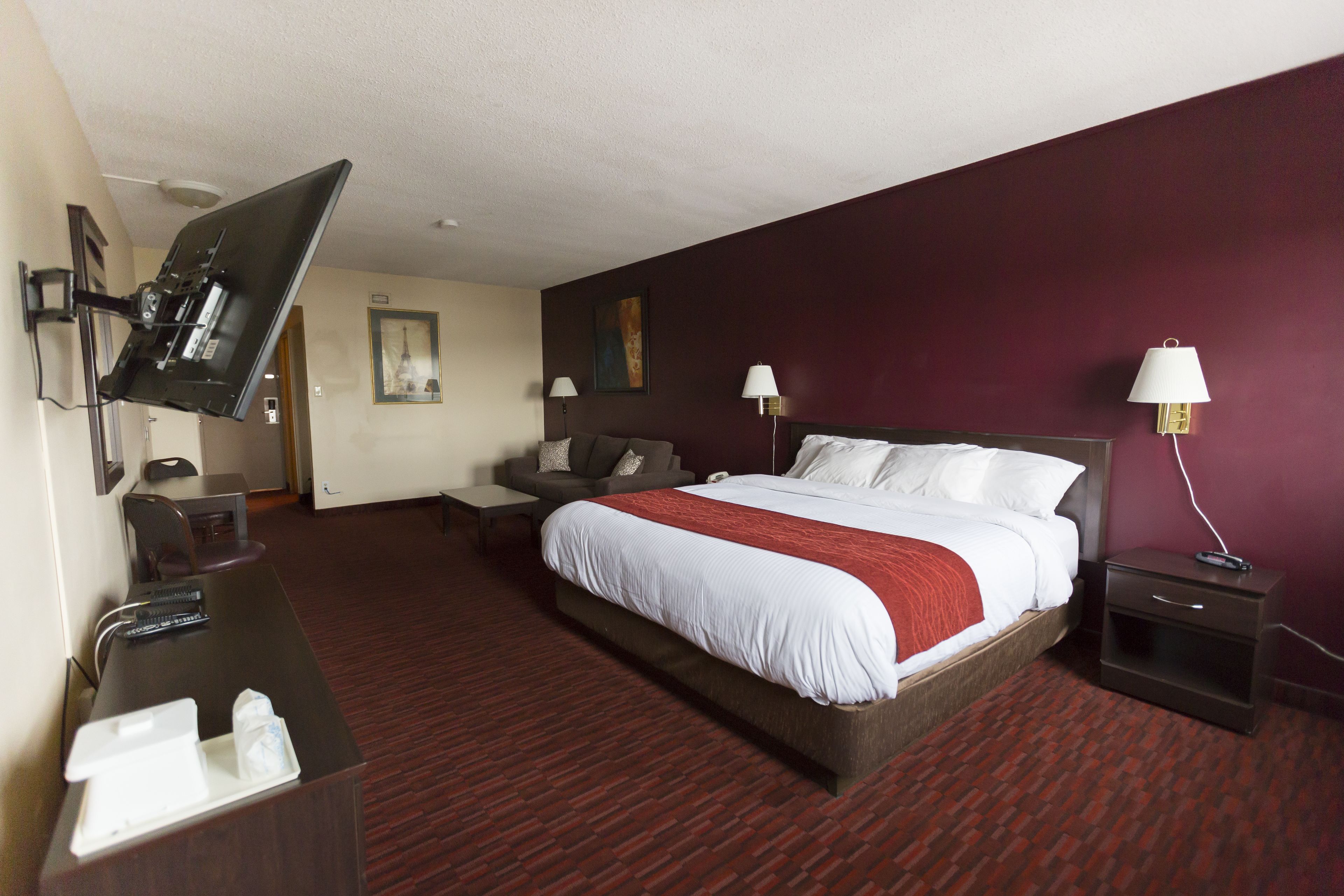 A hotel room with a large bed, a desk with a chair, a TV mounted on the wall, and two bedside lamps.