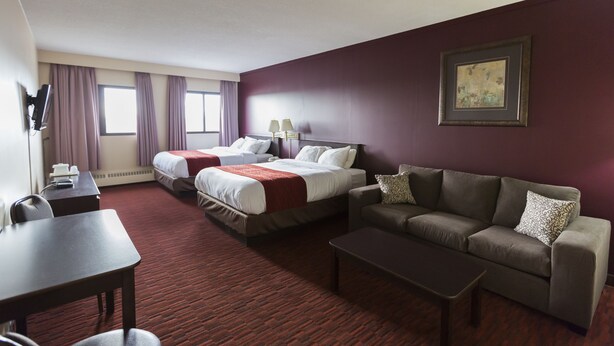 A hotel room with two beds, a sofa, a coffee table, and a TV. - Argyll Plaza Hotel (Edmonton)