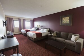 A hotel room with two beds, a sofa, a coffee table, and a TV. - Argyll Plaza Hotel (Edmonton)