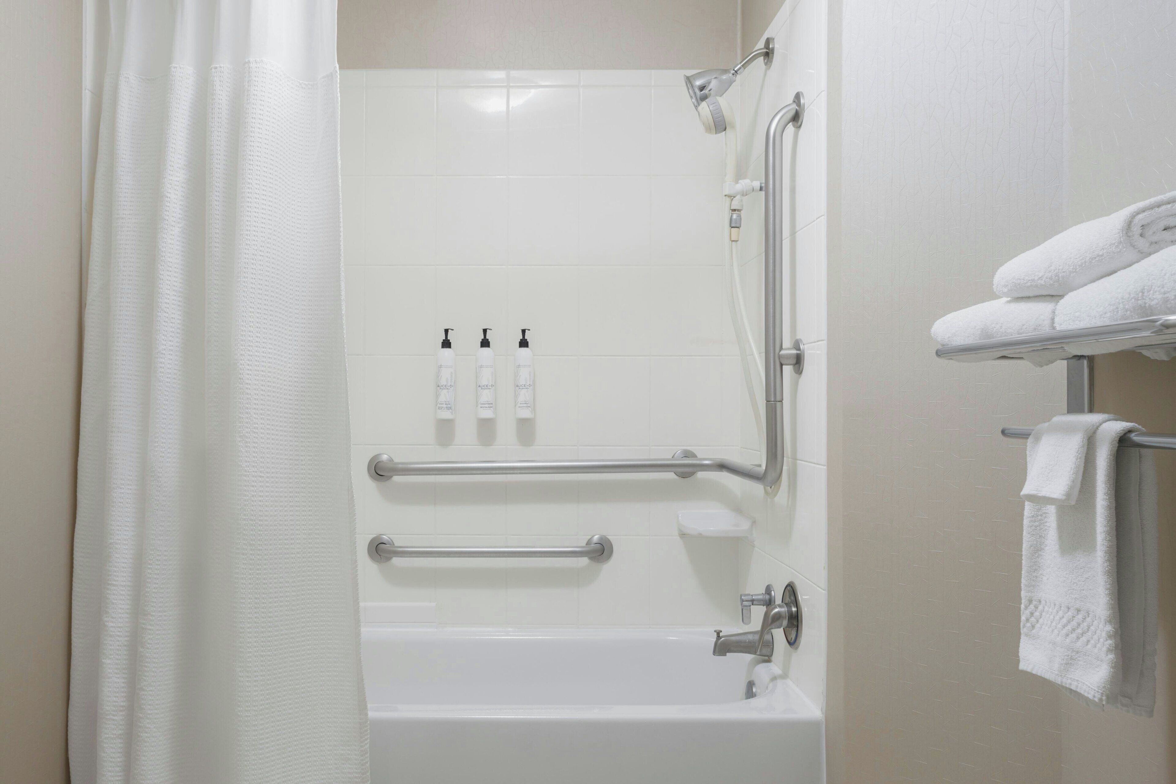 Une salle de bain équipée d’une baignoire, d’une douche, de barres d’appui et d’un porte-serviettes.