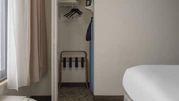 A hotel room with a bed, a small table, a radiator, a coat rack, and a window with curtains.