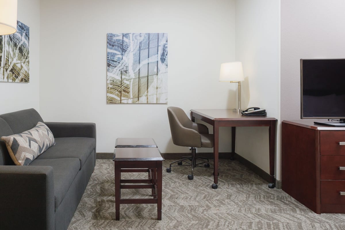 A hotel room with a sofa, a desk, a chair, a TV, and artwork on the walls.