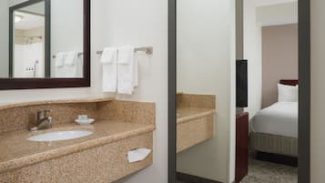 Un baño de hotel con lavamanos de encimera de granito, un espejo y un perchero para toallas.