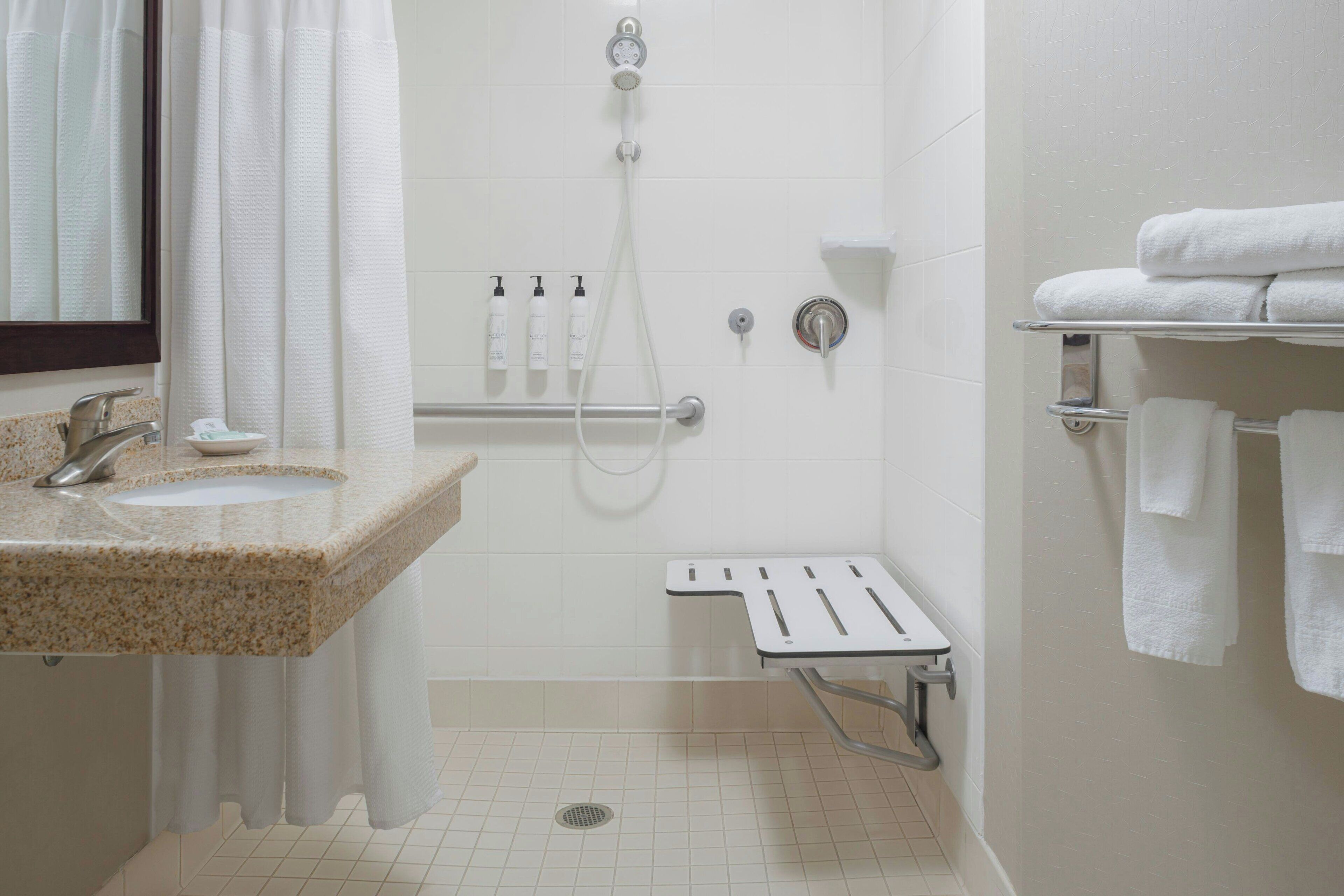 Un baño con lavamanos, ducha, barra de apoyo y toallero.