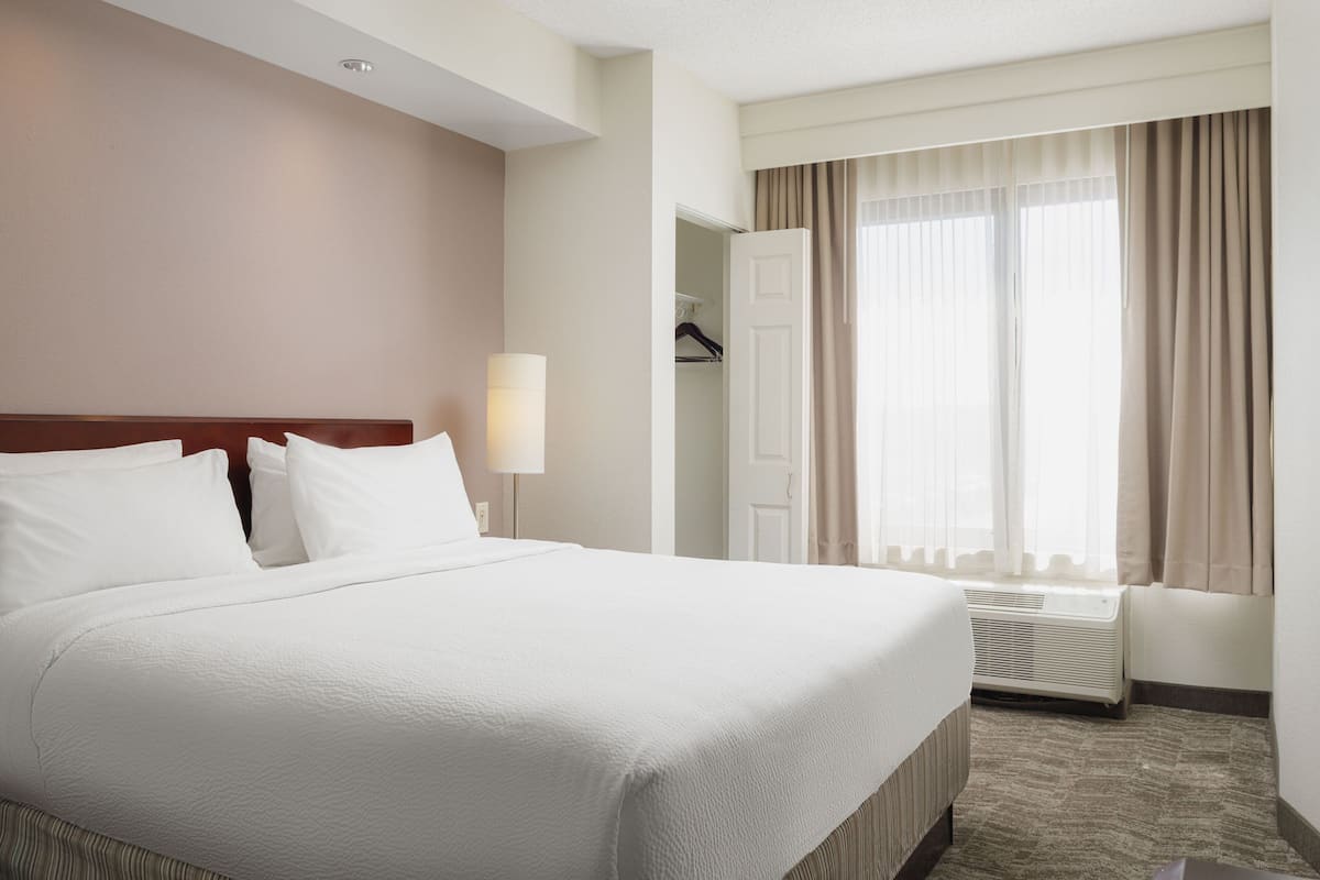 A hotel room with a large bed, a bedside lamp, a window with curtains, and a coat rack.