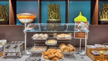 Buffet de café da manhã com diversos pães e doces, uma torradeira e uma placa indicando os pães de café.