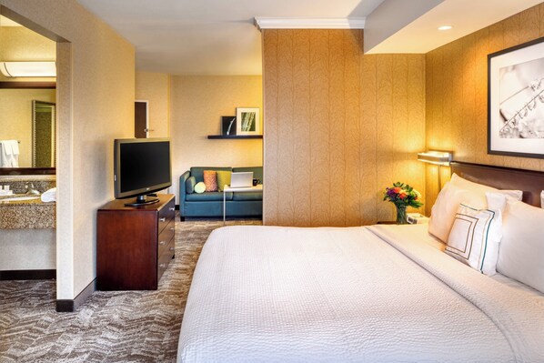 Una habitación de hotel con una cama grande, un televisor de pantalla plana, un sofá, una mesita pequeña y un televisor montado en la pared.