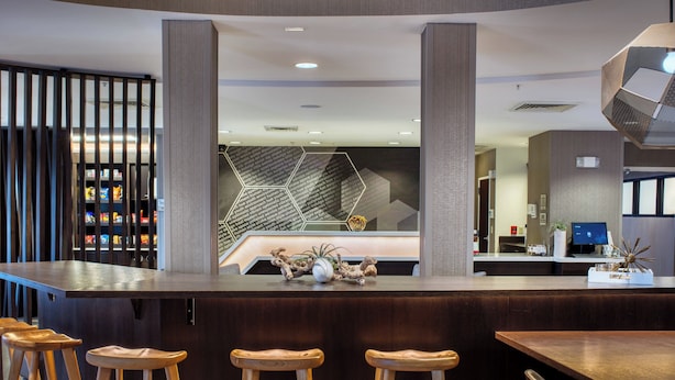A modern reception area with a bar, wooden stools, a decorative plant centerpiece, and a geometric wall design.