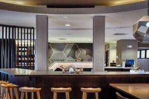 Una moderna zona de recepción con barra, taburetes de madera, un centro de mesa con planta decorativa y un diseño geométrico en la pared.