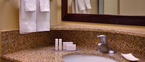 A bathroom with a granite countertop, a sink, a mirror, and two towels hanging on a towel rack.