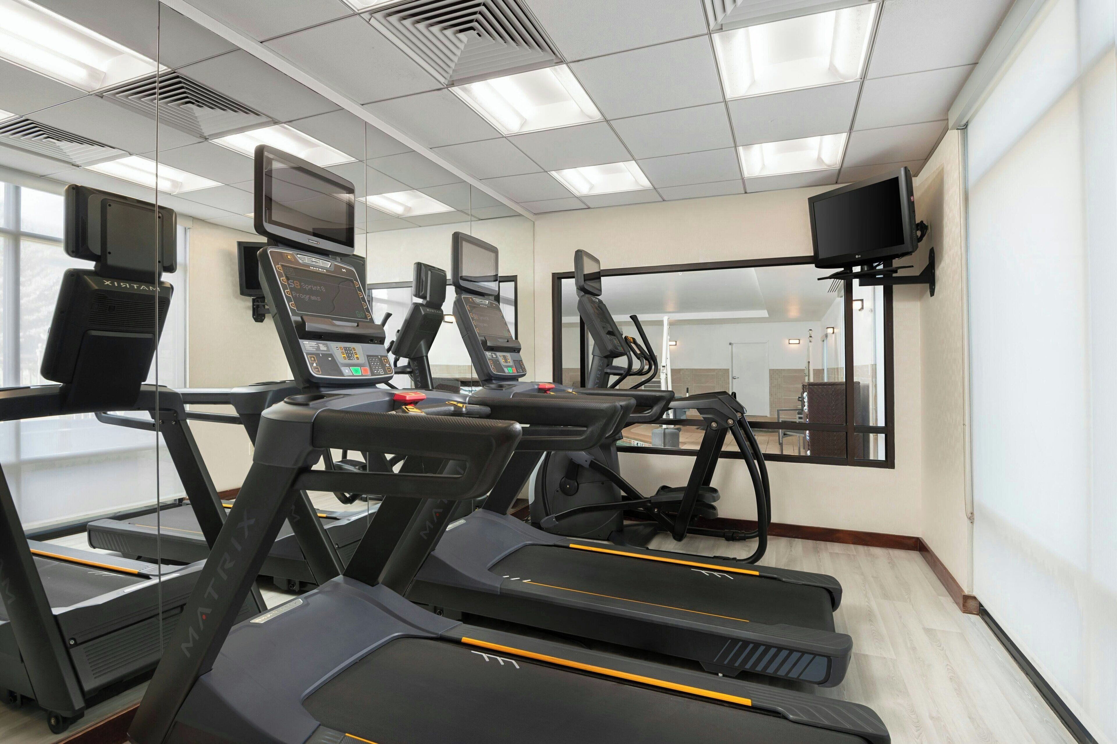 A gym with treadmills, exercise bikes, and a mirrored wall.