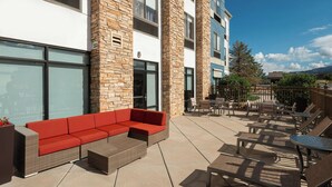 Un espacio al aire libre con patio, un sofá rojo, mobiliario de mimbre y una mesa.
