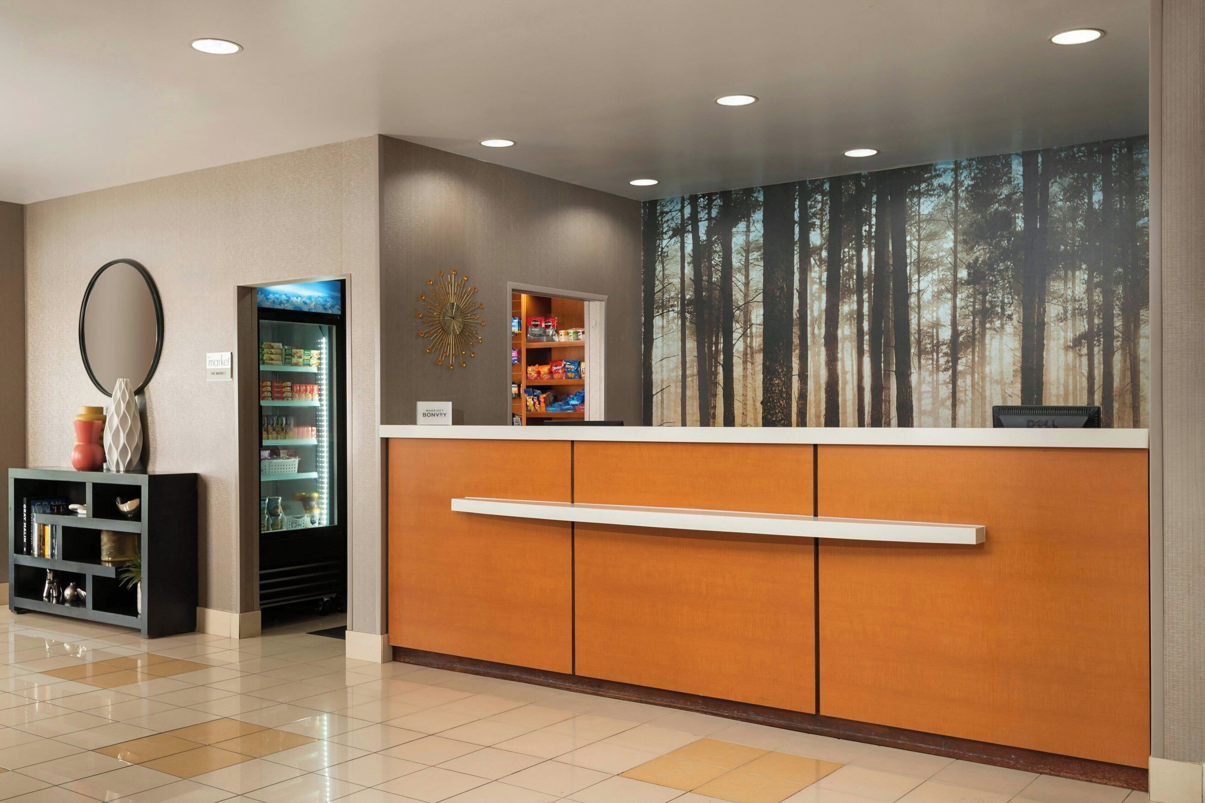 A reception area with a wooden counter, a refrigerator, a bookshelf, and a wall mural of a forest.