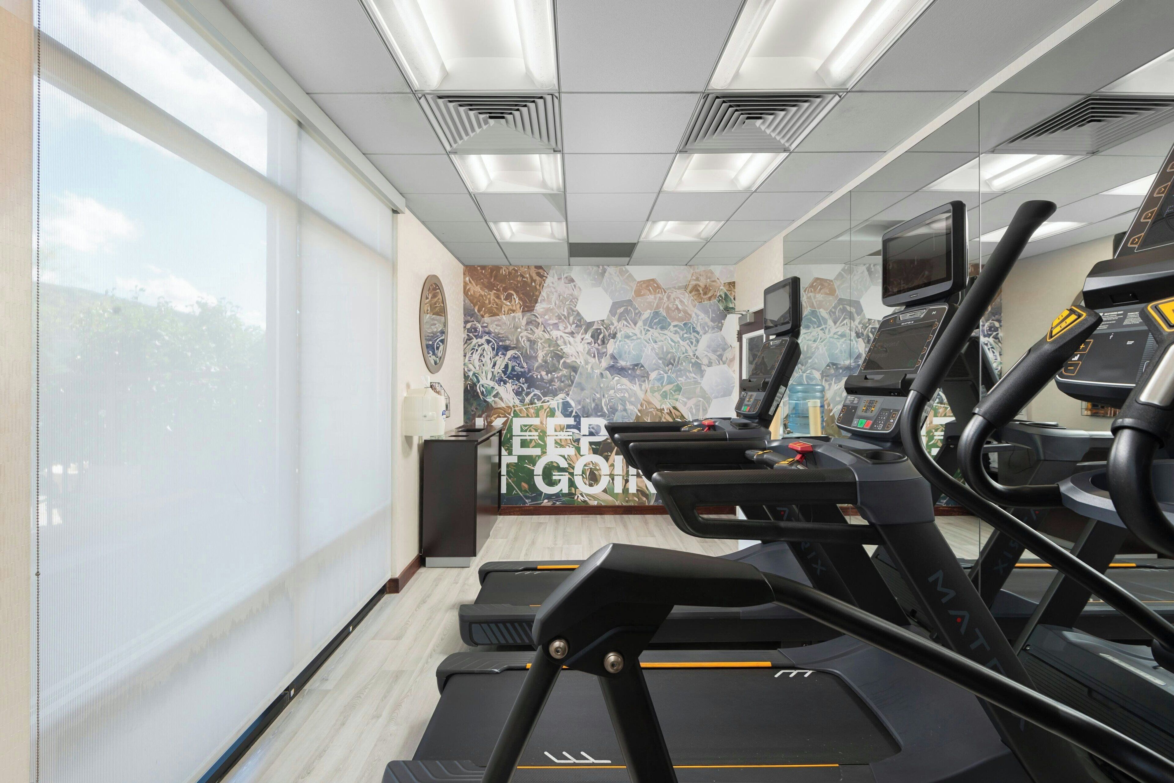 A gym with treadmills, a wall with motivational text, and large windows.
