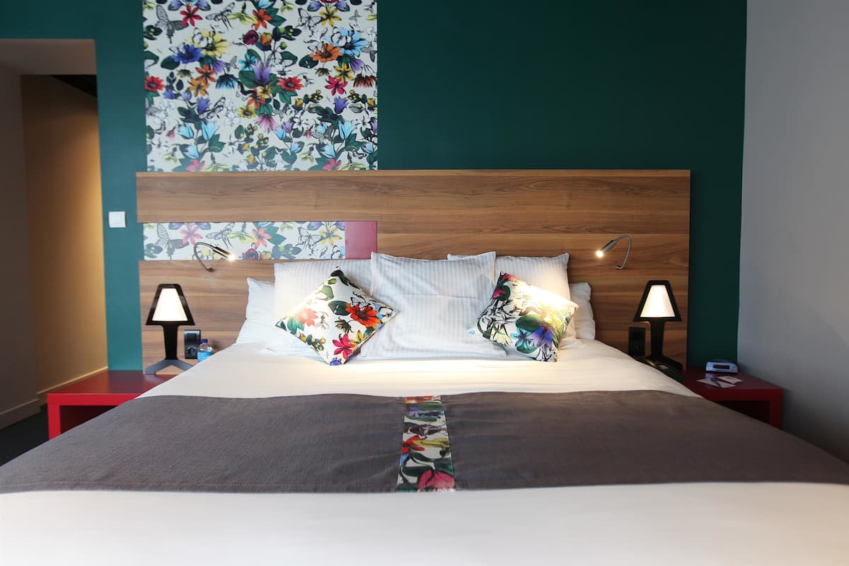 A neatly made bed with floral-patterned pillows, a wooden headboard, and bedside lamps on a red nightstand.